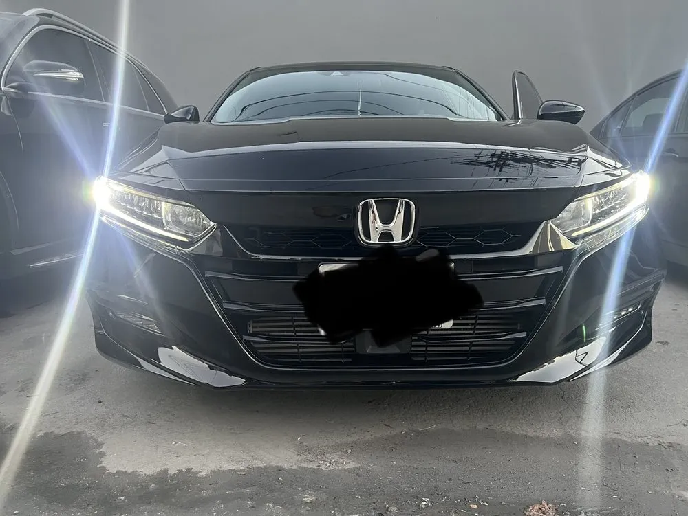 Front of a black Honda Accord sedan with its headlights on
