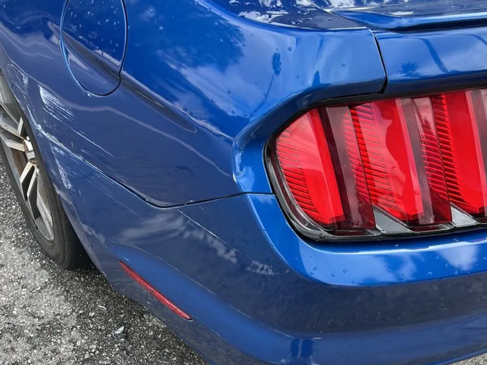 Scuffed rear bumper corner and taillight area on a blue Ford Mustang