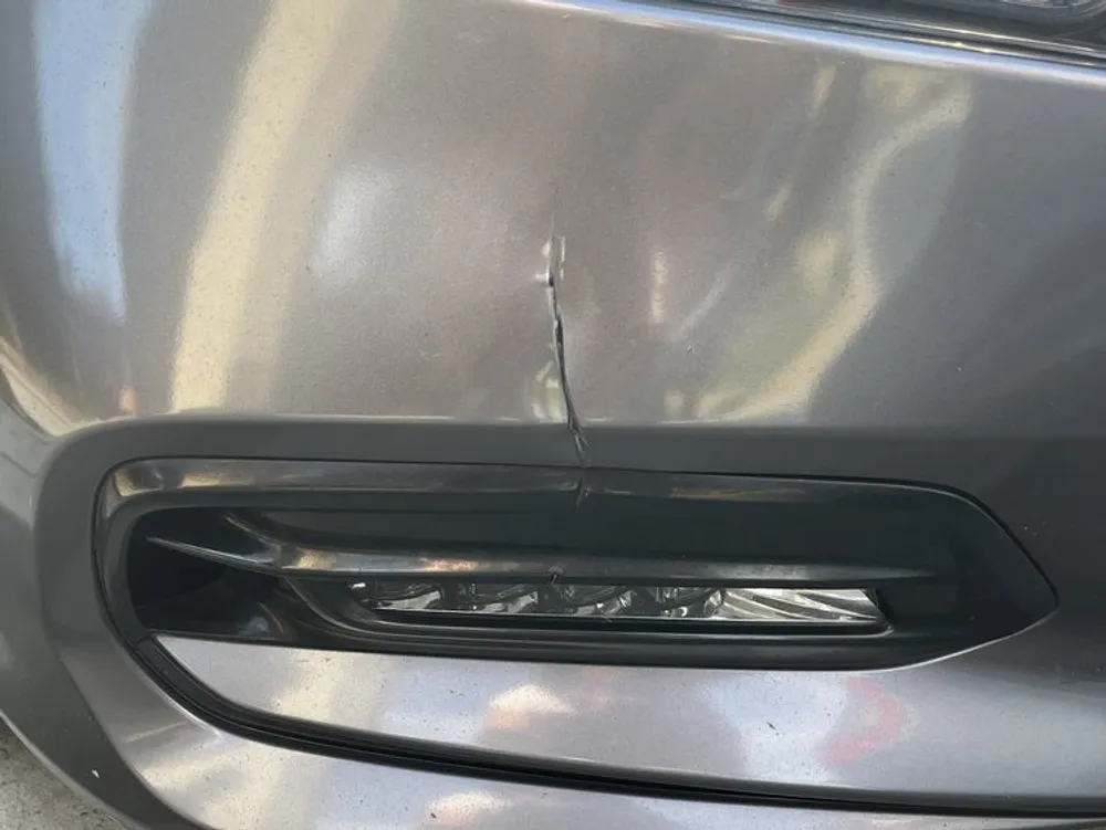 Close-up of a crack in a silver car's bumper above the fog light opening